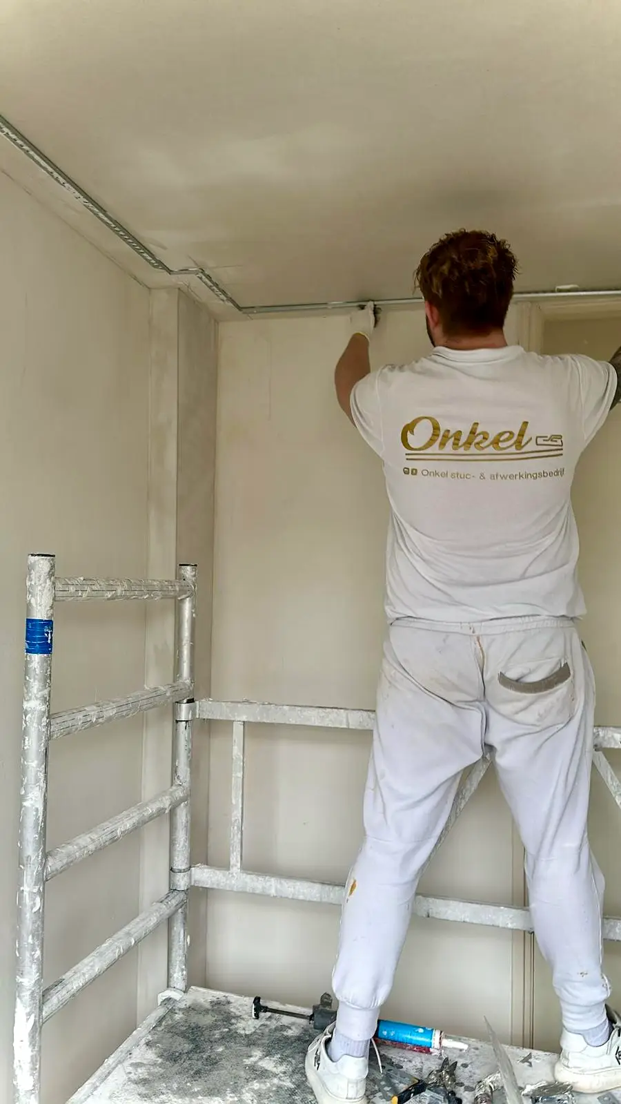 Nigel Onkel aan het werk in zijn Onkel-bedrijfskleding, een muur aan het stuken