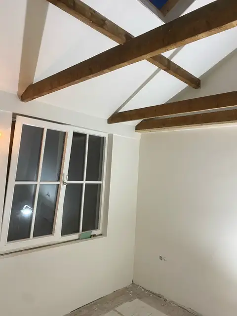 Strak wit stucwerk in een kamer met zichtbare houten dakbalken
