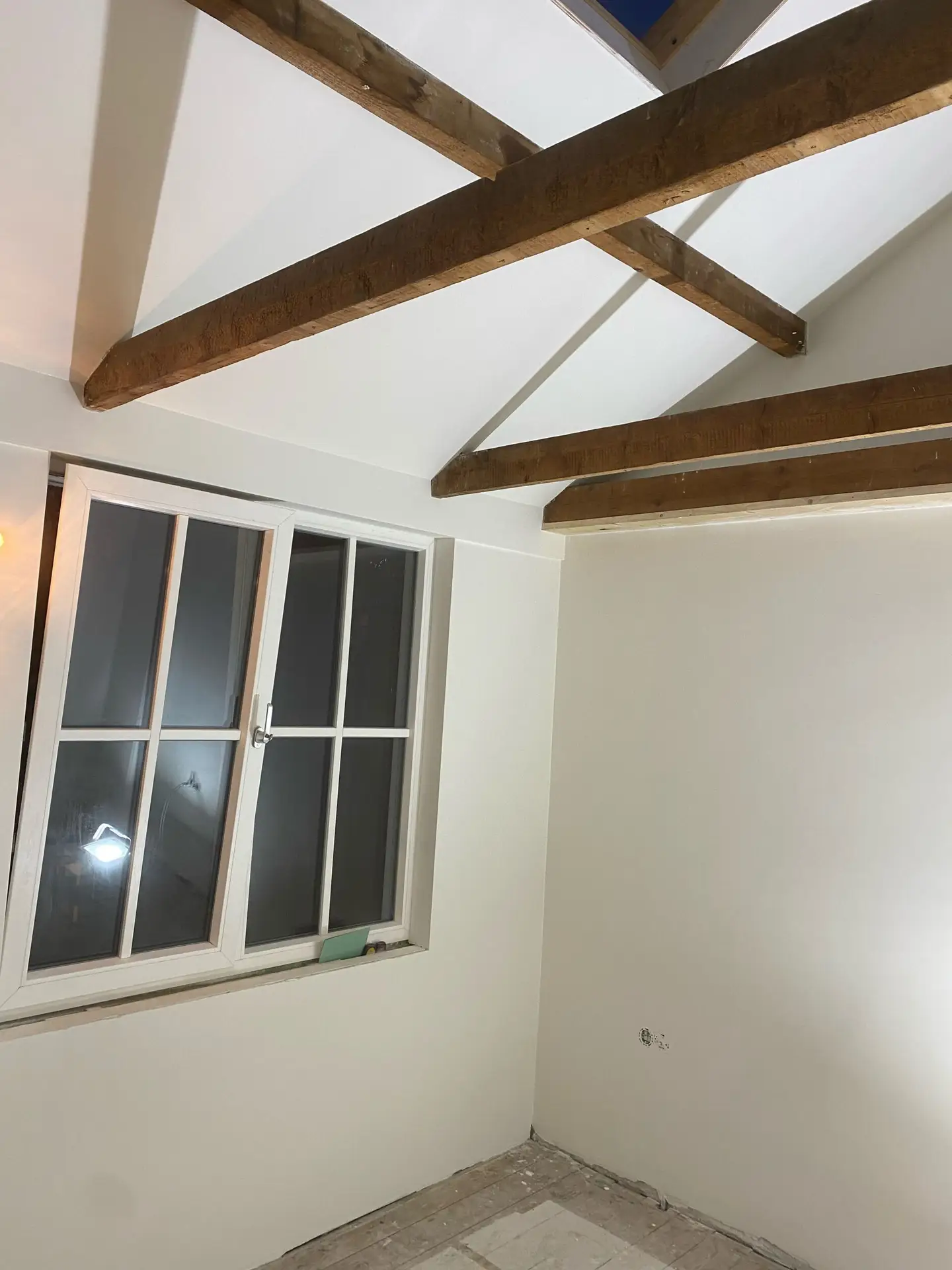 Strak wit stucwerk in een kamer met zichtbare houten dakbalken